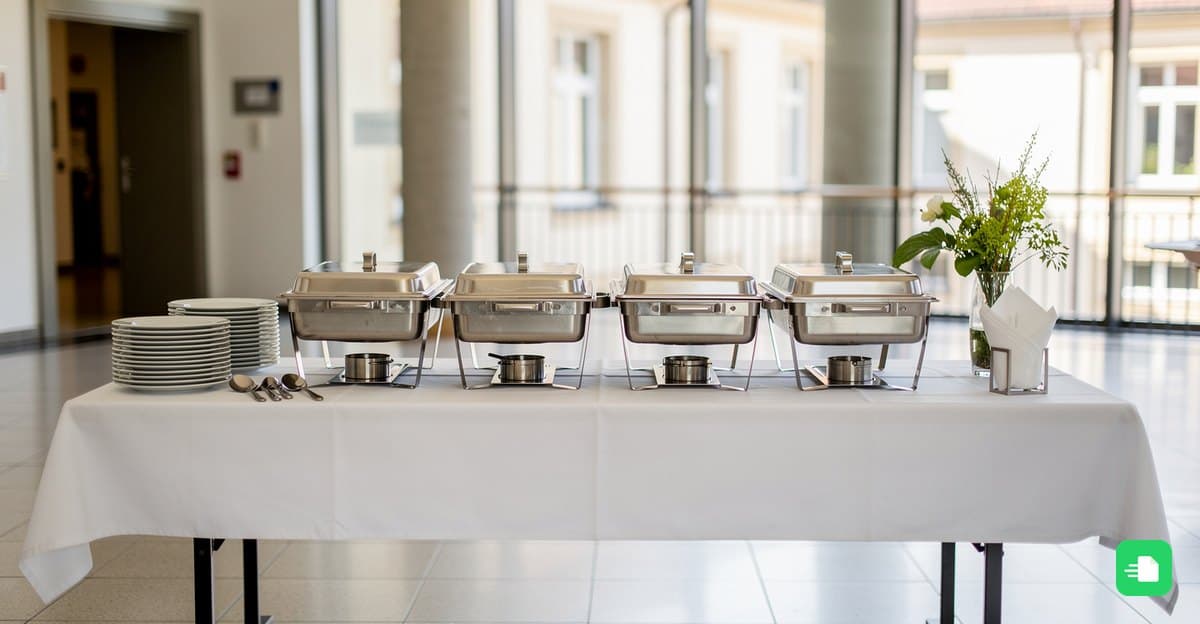 Catering-Buffet mit Warmhaltebehältern und Tellern im hellen Foyer eines öffentlichen Gebäudes